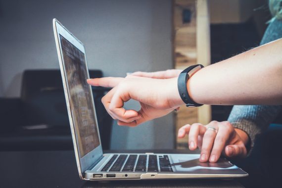 Photo of one person's hands pointing to something on the laptop screen
